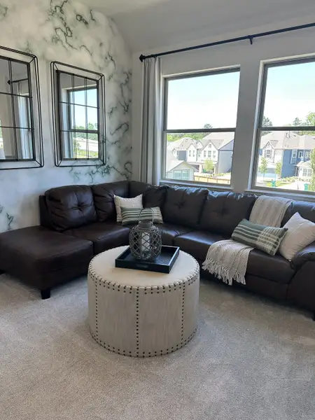 A cozy living room with a leather sectional, marble accent wall, and large windows overlooking suburban homes. A cozy living room with a leather sectional, marble accent wall, and large windows overlooking suburban homes.