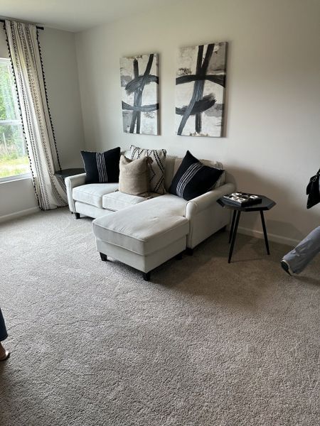 A cozy living room featuring a light gray sectional, abstract art, and soft carpeting.