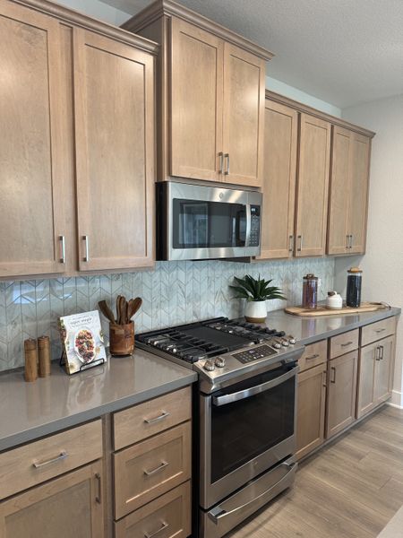 A modern kitchen with sleek wooden cabinets, stainless steel appliances, and a stylish herringbone backsplash.