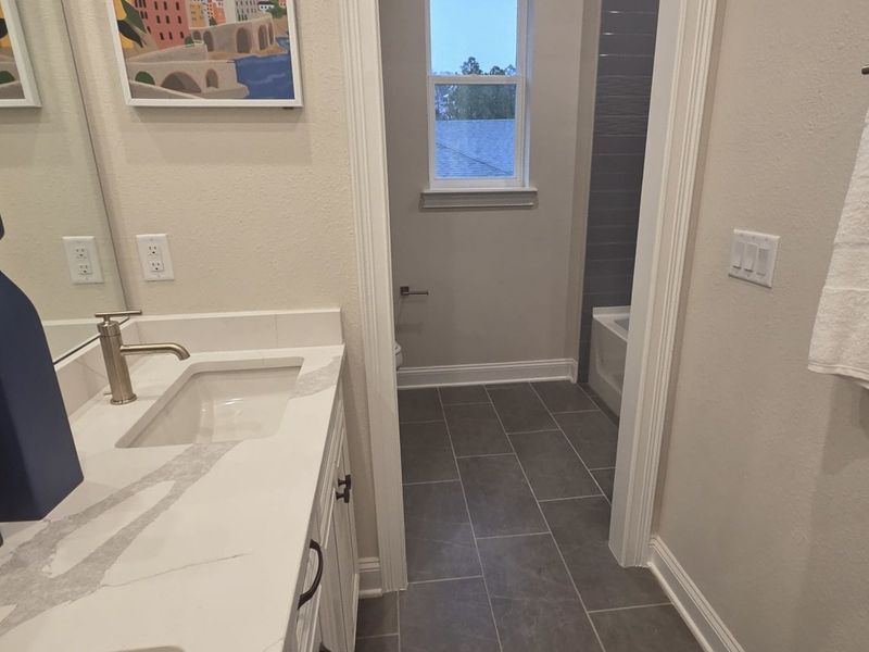 A modern bathroom featuring sleek gray tiles, a chic white vanity with marble accents, and elegant wall art. A modern bathroom featuring sleek gray tiles, a chic white vanity with marble accents, and elegant wall art.