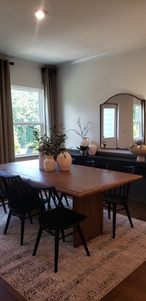 A cozy dining area with a wooden table, black chairs, elegant vases, and a large mirror, accented by natural light.