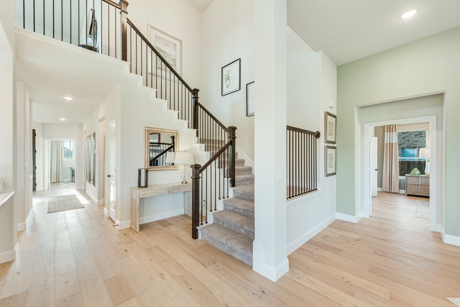 Two-story foyer with carpeted staircase, dark iron railings, and light hardwood floors Two-story foyer with carpeted staircase, dark iron railings, and light hardwood floors