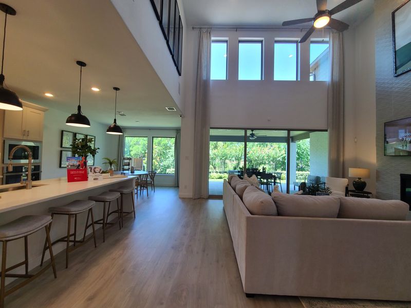 An airy living space with high ceilings, large windows, a sleek kitchen island, and stylish furnishings overlooking a lush backyard.