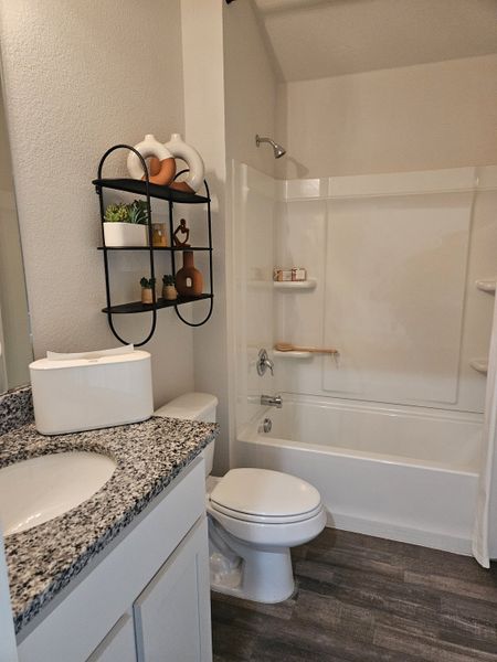 A cozy bathroom with a granite countertop, modern fixtures, and stylish shelving for decor.