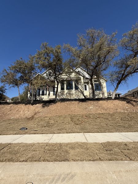 A sophisticated two-story home with a spacious front yard and classic stone facade in Lakeside at Tessera by Coventry Homes (Lago Vista, TX).