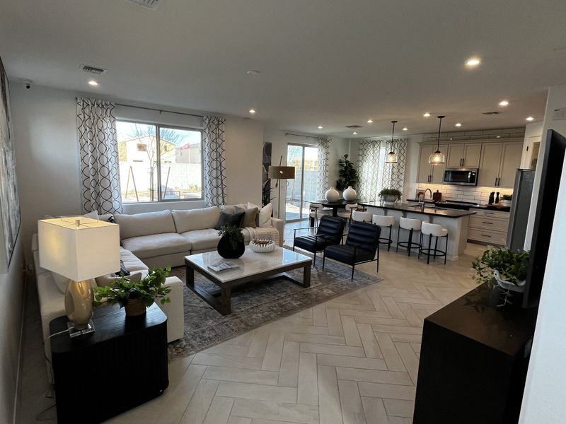 Elegant living area with a white sectional, black chairs, and an open-concept kitchen with pendant lighting and neutral tones.