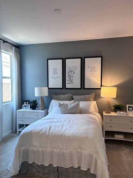 A cozy bedroom with a plush bed, soft gray walls, elegant artwork, and soft lighting from twin bedside lamps.