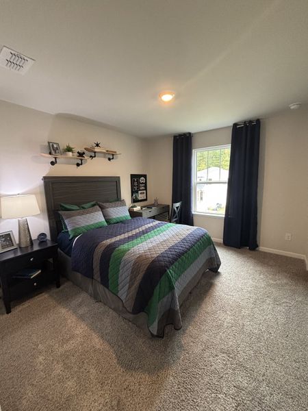 A cozy bedroom with a striped quilt, dark curtains, and modern decor on a soft carpeted floor.