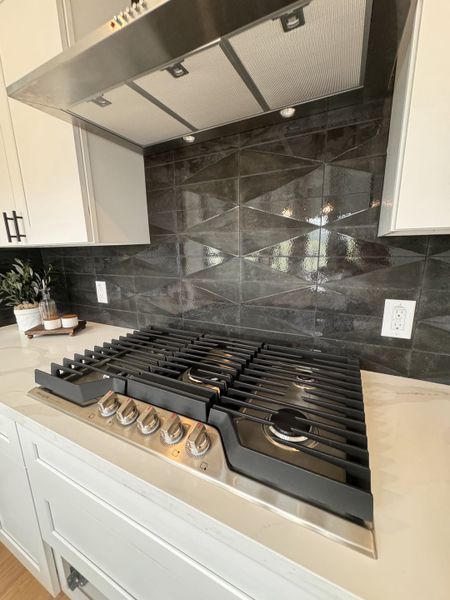 A modern kitchen with a sleek black tile backsplash, stainless steel range hood, and a gas stove with elegant white cabinetry. A modern kitchen with a sleek black tile backsplash, stainless steel range hood, and a gas stove with elegant white cabinetry.