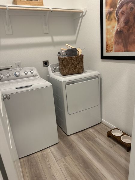 A functional laundry room featuring a washer, dryer, wood floors, and a shelf with a charming woven basket. A functional laundry room featuring a washer, dryer, wood floors, and a shelf with a charming woven basket.