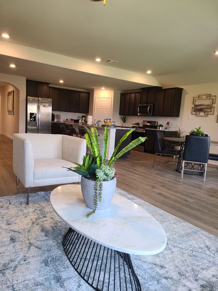 Open-concept living area with modern kitchen, cozy seating, and wooden flooring, accented by stylish decor.