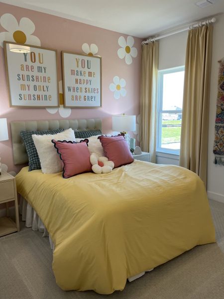 A cheerful bedroom with a yellow quilt, floral decor, soft cushions, and natural light filtering through beige curtains. A cheerful bedroom with a yellow quilt, floral decor, soft cushions, and natural light filtering through beige curtains.