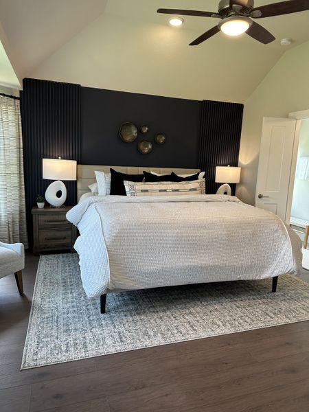 A cozy bedroom with a plush bed, textured dark accent wall, modern lighting, and a stylish neutral rug. A cozy bedroom with a plush bed, textured dark accent wall, modern lighting, and a stylish neutral rug.