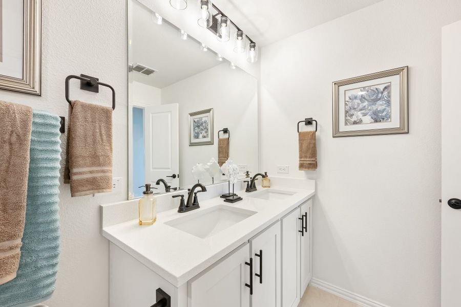 Bathroom with double sink vanity, white cabinets, black fixtures, and large mirror with track lighting above