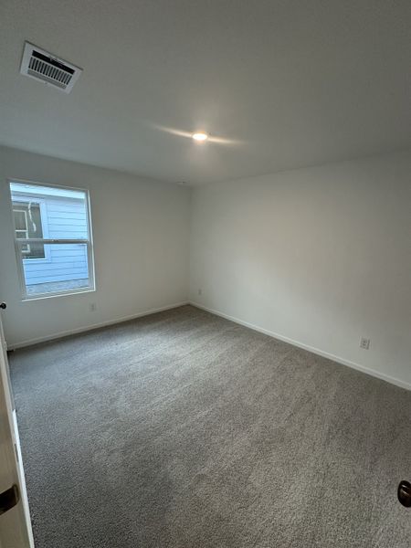 A bright, carpeted room with a window and recessed lighting, featuring neutral walls and ceiling.