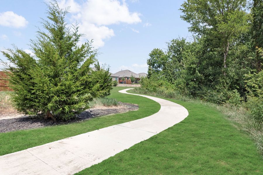Curved concrete walking path through green lawn with trees and a home visible in the background