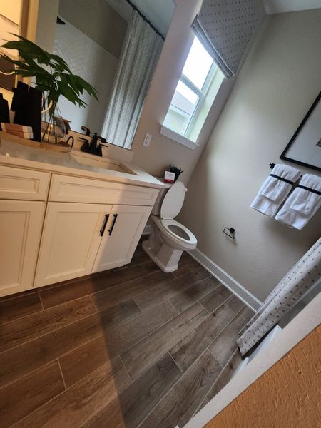 A chic bathroom with wood-style flooring, white vanity, and modern fixtures, offering elegance and comfort. A chic bathroom with wood-style flooring, white vanity, and modern fixtures, offering elegance and comfort.