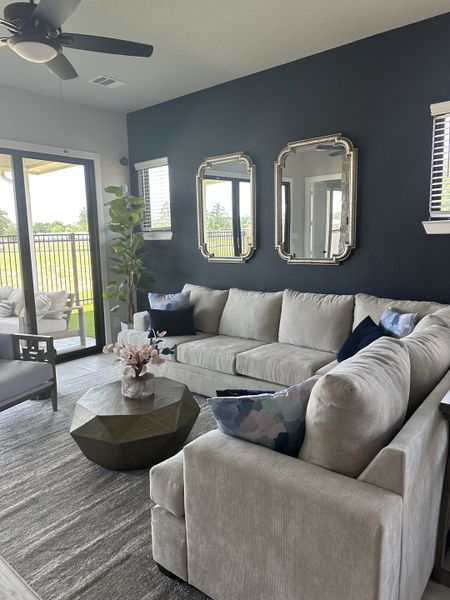 Modern living room with a chic gray sofa, geometric coffee table, and dark accent wall with mirrors, overlooking a scenic view.