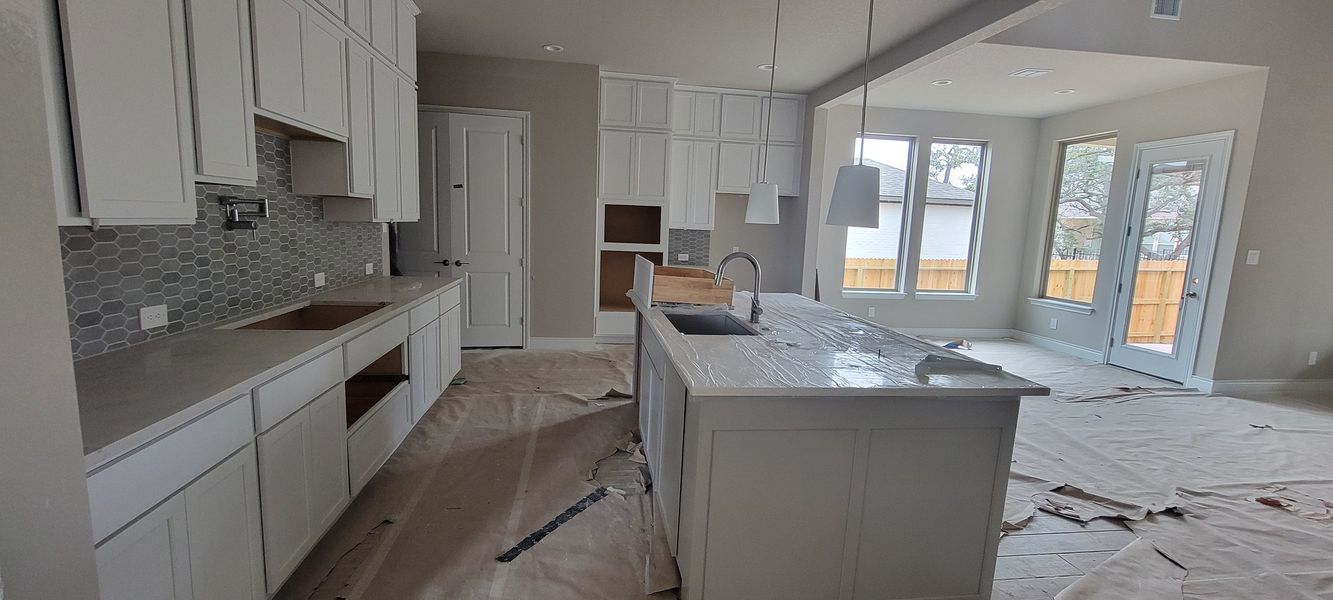 A modern kitchen with white cabinetry, a sleek island, gray hexagonal tile backsplash and pendant lighting.