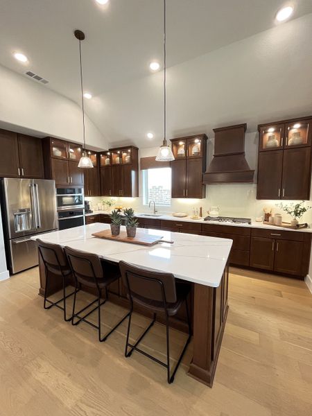 A modern kitchen featuring dark wood cabinets, a spacious island with pendant lighting, and stainless steel appliances.