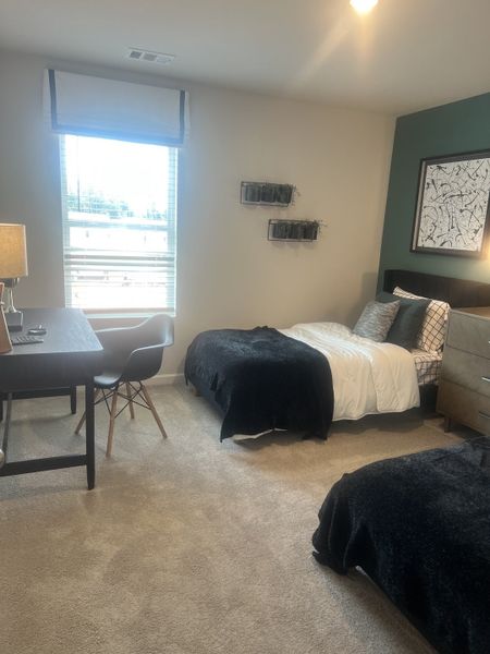 A cozy bedroom features twin beds with dark bedding, a study desk, chic decor, and a large window for natural light.