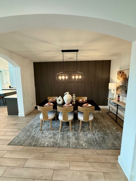 A modern dining room with a dark accent wall, elegant chandelier, and wooden chairs around a sleek table.