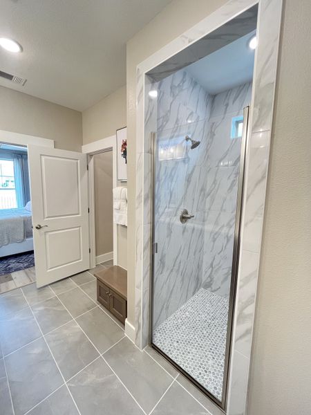 A modern bathroom with a marble shower, gray floor tiles, and elegant decor, leading to a cozy bedroom. A modern bathroom with a marble shower, gray floor tiles, and elegant decor, leading to a cozy bedroom.