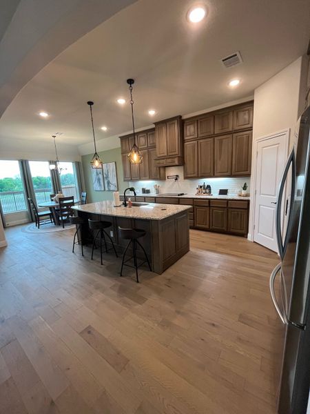 A spacious kitchen with wooden cabinets, an island, pendant lighting, and hardwood floors, leading to a dining area with large windows. A spacious kitchen with wooden cabinets, an island, pendant lighting, and hardwood floors, leading to a dining area with large windows.