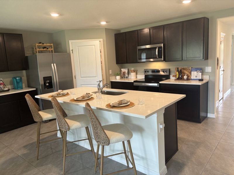 Modern kitchen featuring dark cabinets, sleek appliances, and a white island with chic seating for casual dining.
