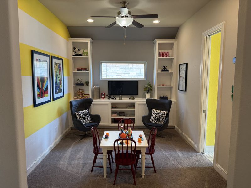 A vibrant playroom with yellow accents, built-in shelves, chic artwork, and cozy seating facing a small activity table.