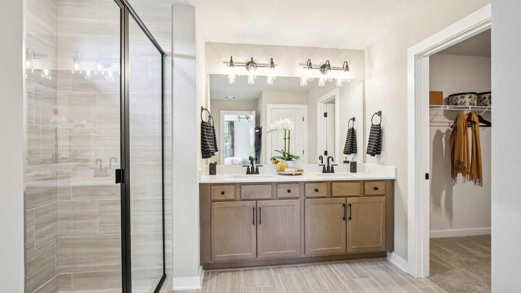Large bathroom with tiled shower in glass enclosure, dual vanity, and primary closet