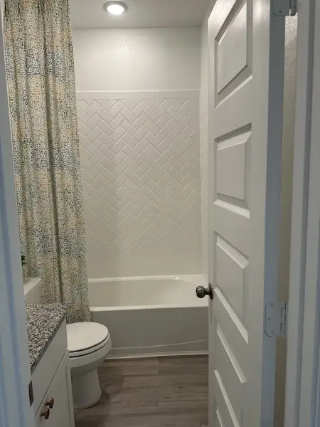 A cozy bathroom with a herringbone-tiled bathtub, speckled granite countertop, and warm wood flooring.
