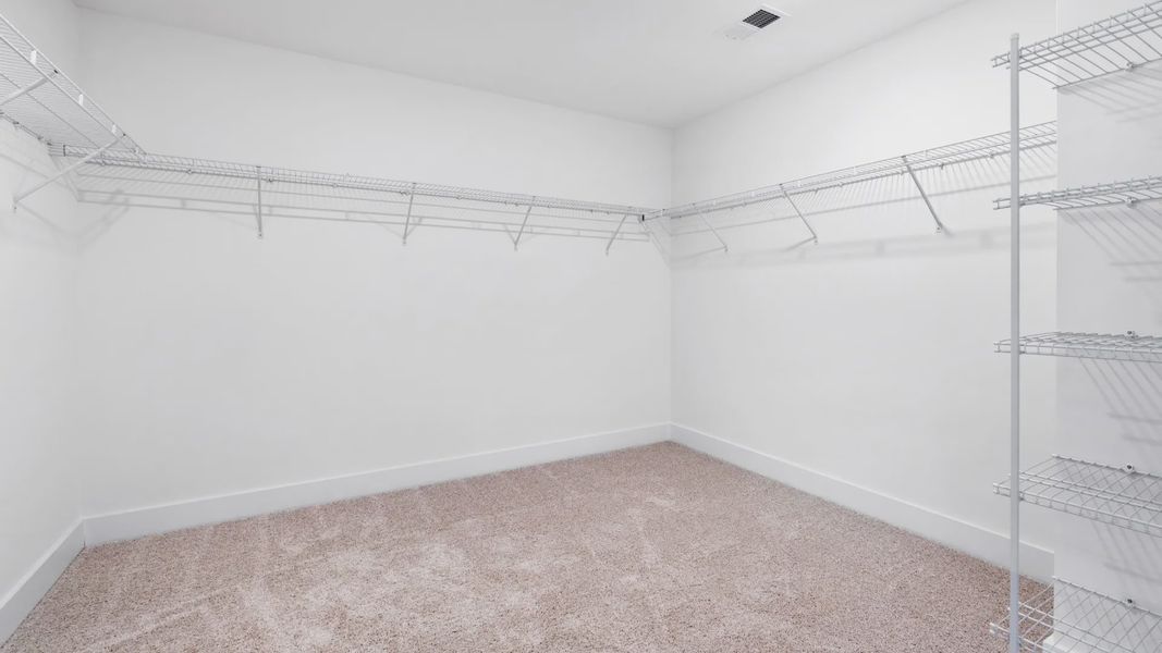 Large walk-in closet in primary suite with included shelving, hanging room & carpeted flooring at Magnolia Park by DRB Homes Large walk-in closet in primary suite with included shelving, hanging room & carpeted flooring at Magnolia Park by DRB Homes