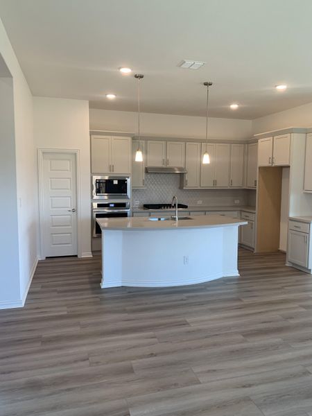 A modern kitchen with light cabinets, pendant lighting, stainless steel appliances, and hardwood flooring. A modern kitchen with light cabinets, pendant lighting, stainless steel appliances, and hardwood flooring.
