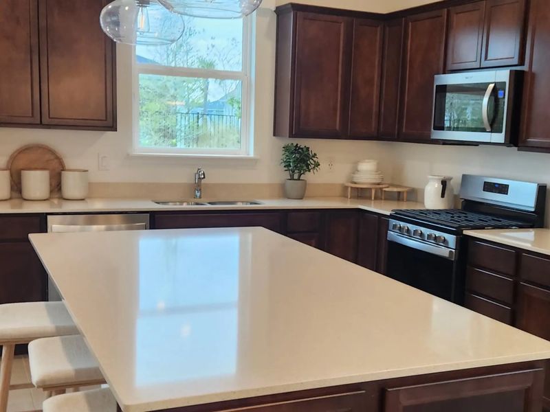 A modern kitchen with rich wood cabinetry, sleek countertops, stainless steel appliances, and elegant pendant lighting.