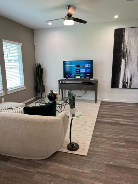 A modern living room with a sleek white couch, wood floors, minimalist decor, and a wall-mounted TV.