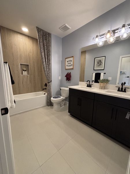 A stylish bathroom featuring a blue accent wall, a classic white vanity, and a tiled bathtub in Eden at Crossprairie by M/I Homes (St. Cloud, FL).