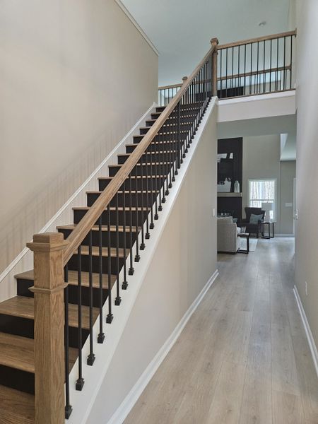A modern staircase with wooden steps, black railings, and a white wall, leading to an open upper floor.
