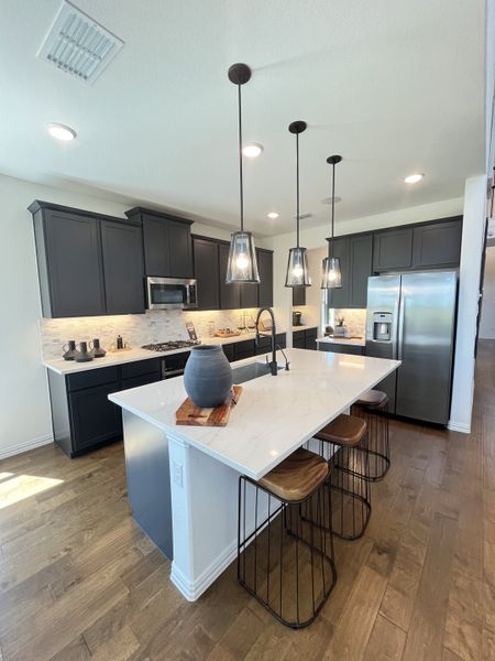 A modern kitchen with dark cabinets, pendant lights, a sleek island, and stainless steel appliances.