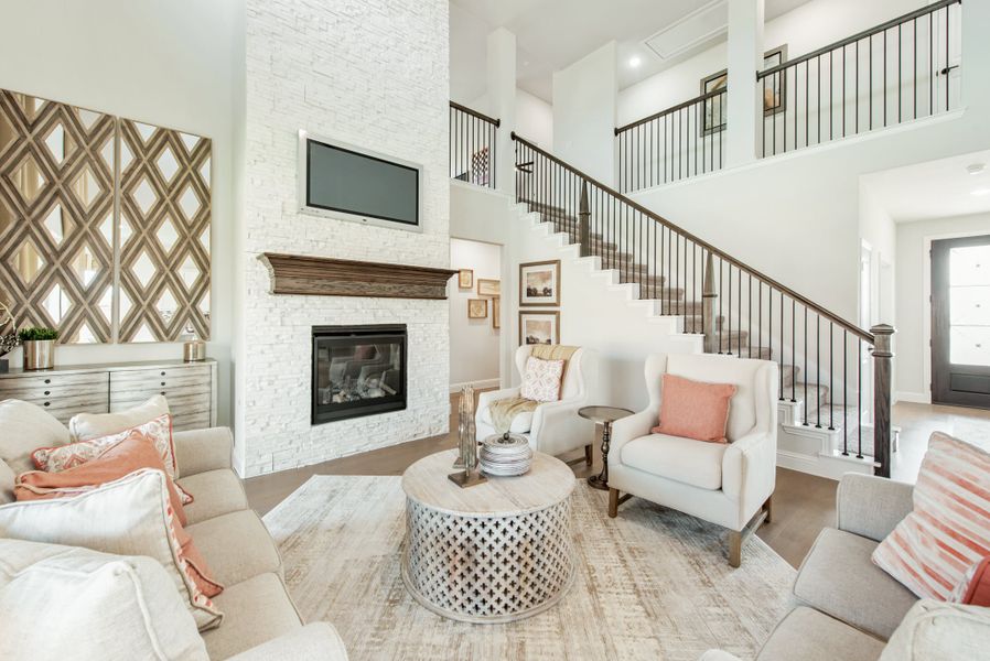 Living room with two-story ceiling, white stone fireplace, staircase, and neutral furniture with coral accents