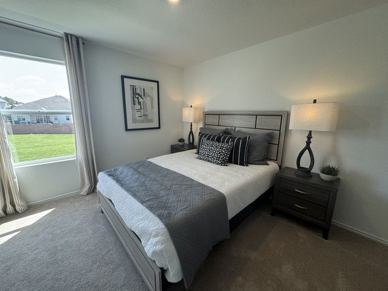 A cozy bedroom with a modern bed, stylish lamps, and large window overlooking a green lawn. Elegant decor with neutral tones.