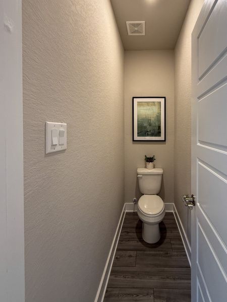 A cozy powder room with wood-look flooring, neutral walls, and elegant artwork above the toilet.