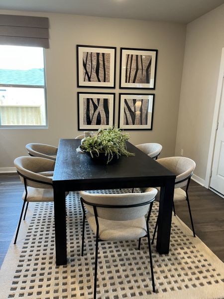 A modern dining area featuring a sleek black table, cozy chairs, and abstract art on the walls.