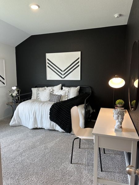 A chic bedroom with a black accent wall, cozy white bedding, and a modern desk setup with stylish decor.