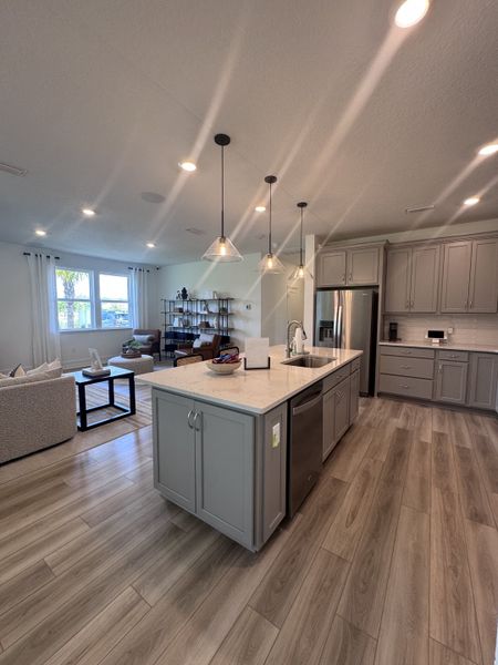 A modern kitchen with sleek lighting, gray cabinetry, and an island featuring a breakfast bar and light wood flooring.