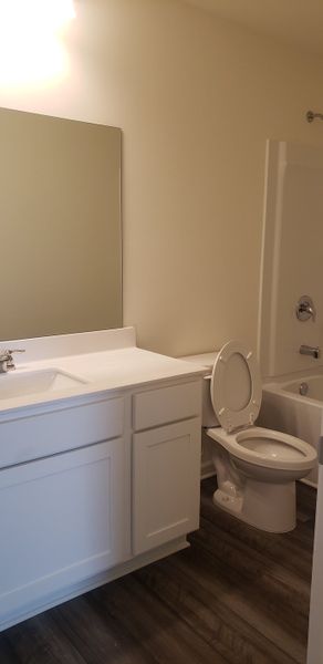 A bright bathroom with sleek white cabinetry, a large mirror, and warm wood flooring.