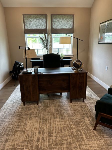 A cozy home office featuring a wooden desk, neutral decor, ample natural light, and an elegant area rug.
