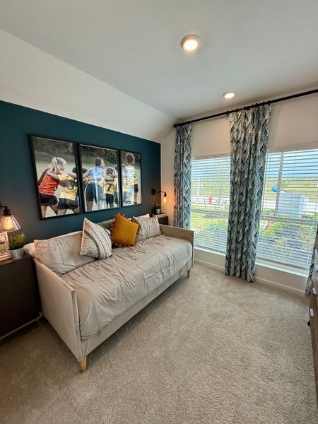 A cozy room featuring a plush daybed, vibrant cushions, and large windows with stylish curtains and modern artwork.