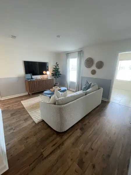 A cozy living room with elegant wood flooring, a plush sofa, and a modern entertainment setup. Neutral tones and stylish decor.