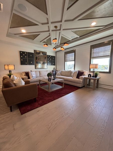 A sophisticated living room with a coffered ceiling, stylish lighting, and plush seating in Eden at Crossprairie by M/I Homes (St. Cloud, FL).